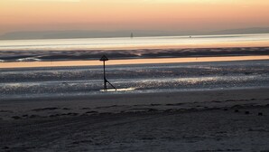 Una playa al atardecer con cielo despejado, aguas tranquilas y una orilla distante.