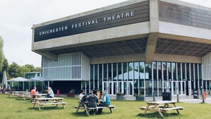 Un edificio moderno con un cartel que dice "Chichester Festival Theatre" y zonas de estar al aire libre.