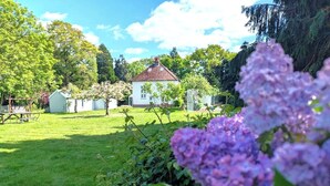 Un cementerio con un edificio blanco, césped verde y flores moradas en primer plano.