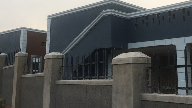 Um edifício com fachada escura, entrada saliente no canto e área cercada por grade de metal.