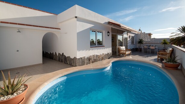 A modern house with a swimming pool, outdoor furniture, and a patio area.