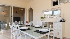 A dining area with a glass table, white chairs, and a white cabinet with a mirror and clock.