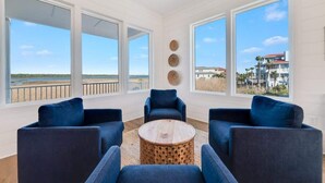 Una habitación amplia con grandes ventanales, una mesa de centro redonda de madera y sillas tapizadas en azul.