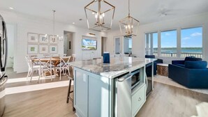 Una cocina moderna con una isla central, un comedor con sillas blancas y una sala de estar con sofás azules.