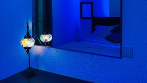 Una habitación con cama, mesita de noche, espejo y lámpara de pared.