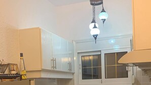 Cocina compacta con armarios blancos, horno empotrado, pileta y una ventana sobre la pileta.
