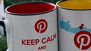Dos tazas con el logotipo de Pinterest y el texto “KEEP CALM AND” en un balcón con vistas a follaje y un paisaje lejano.