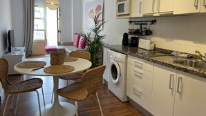 Ett modernt kök med en inbyggd tvättmaskin, en mikrovågsugn och en diskho. Det finns en matplats med flätade stolar och ett runt bord.