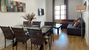 A modern living room with a dining area, featuring a glass-top table, wicker chairs, a grey sofa, and a floor lamp. - Malaga Center Flat Cathedral Balcony City Views (Málaga)