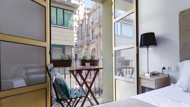 A hotel room with a bed, a desk with a lamp, a chair, a small table with a plant, and a balcony with a chair and a table. - Malaga Center Flat Cathedral Balcony City Views (Málaga)