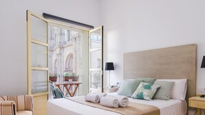 A hotel room with a bed, a chair, a nightstand, and a window with a view of buildings. - Malaga Center Flat Cathedral Balcony City Views (Málaga)