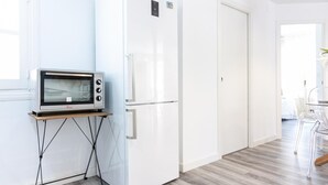 Een moderne keuken met een ingebouwde magnetron, een witte koelkast en een houten eettafel met stoelen.