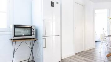 Une cuisine moderne équipée d’un four à micro-ondes encastré, d’un réfrigérateur blanc et d’une table à manger en bois avec des chaises.