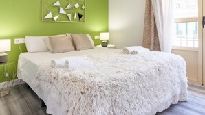 Een hotelkamer met een groene accentmuur, een geometrische spiegel, een zachte witte plaid en uitzicht op buiten door een raam.