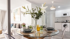 Een moderne eethoek met een glazen tafel, transparante stoelen en een vaas met bloemen.