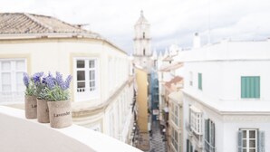 Ein Balkon mit Lavendelsträuchern und Blick auf eine enge Straße mit Gebäuden und einem Turm in der Ferne.