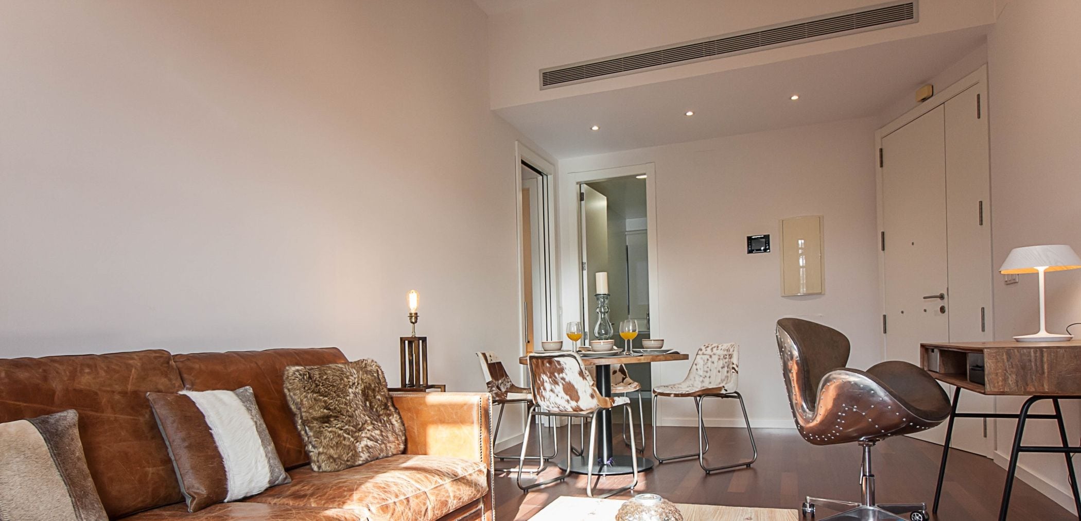 Uma sala de estar moderna com um sofá de couro, uma mesa de centro de madeira e um espaço de refeições com cadeiras e mesa.