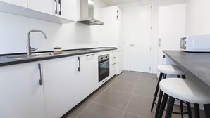 A modern kitchen with white cabinets, a stainless steel range hood, a built-in oven, a microwave, and a bar stool. - Malaga Luxury City Center. Parking (Málaga)