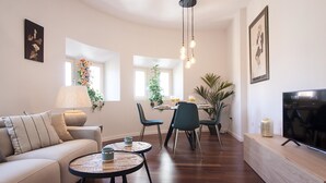 A modern living room with a sofa, coffee table, TV, and dining area with chairs and a plant. - Malaga Luxury City Center. Parking (Málaga)