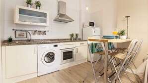 Cocina compacta con lavadora, horno, microondas y comedor con sillas y una mesa.