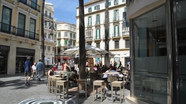 Un área de café al aire libre con mesas y sillas, rodeada de edificios con ventanas amplias y balcones.
