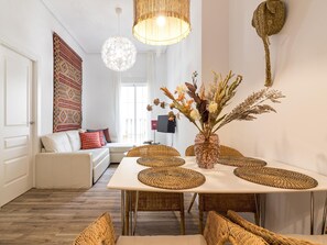 Uma sala de estar moderna com um sofá branco, uma mesa de jantar com jogos americanos trançados e um vaso decorativo com flores secas.