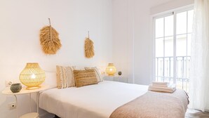 Ein Schlafzimmer mit einem großen Bett, zwei Wandlampen, einem kleinen Nachttisch und einem Balkon mit weißen Vorhängen.