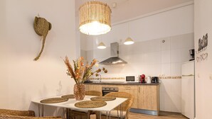 Eine moderne Küche mit Essbereich, ausgestattet mit Rattanmöbeln, einem weißen Tisch und einer Dekovase mit Trockenblumen.