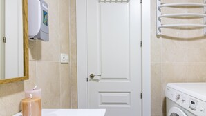 Ein Badezimmer mit einer weißen Tür, einem Handtrockner, einem Handtuchhalter, einer Waschmaschine und einer Kerze am Waschbecken.