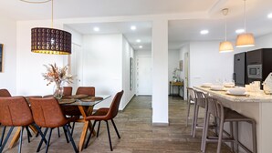 A modern kitchen with a central island, a dining area with a glass table, and a hallway leading to another room. - Malaga Exclusive Beach Apartment with Terrace (Málaga)