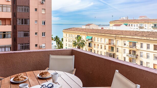 A balcony with a wooden table, chairs, and a view of the sea and buildings. - Malaga Exclusive Beach Apartment with Terrace (Málaga)