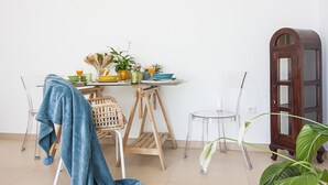 Um quarto com uma mesa de jantar posta com diversos pratos e bebidas, uma cadeira de vime, um cobertor azul e um armário de madeira.