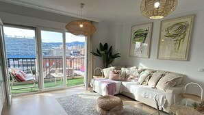 Uma sala de estar moderna com um sofá, uma mesa de centro e uma grande janela com vista para edifícios e uma varanda.