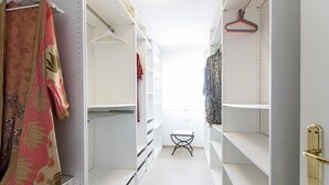 Um closet estreito com prateleiras brancas, um banquinho pequeno e cabides na parede.