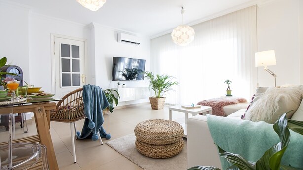 Uma sala de estar moderna com área de jantar, televisão na parede e uma grande janela com cortinas.