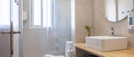 A modern bathroom with a glass-enclosed shower, a toilet, a sink, and a mirror.