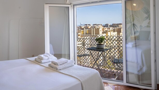 A hotel room with a bed, a balcony with a table and a potted plant, and a view of the cityscape. - Apartamento con Balcon. Free Parking (Málaga)