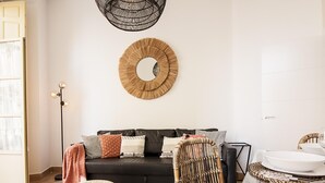 Een moderne woonkamer met een zwarte bank, een ronde wanddecoratie van geweven materiaal, rieten meubels en een glazen eettafel.