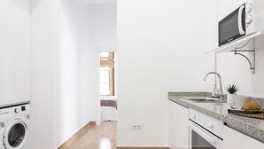 Een moderne keuken met witte kasten, een ingebouwde magnetron, een spoelbak en een klein aanrecht met een plant en een croissant.