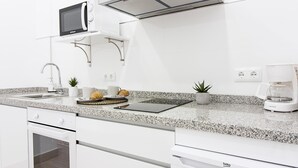 Een moderne keuken met witte kastjes, een ingebouwde magnetron, een koffiezetapparaat en een kleine plant in een pot.