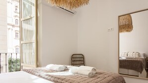 Een slaapkamer met een groot bed, een houten stoel, een spiegel en een raam met gordijnen.