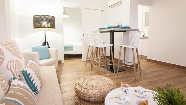 Ein modernes Wohnzimmer mit einer Couch, einem Esstisch mit Stühlen, einer Lampe und einem kleinen runden Tisch mit Tassen und einer Pflanze.