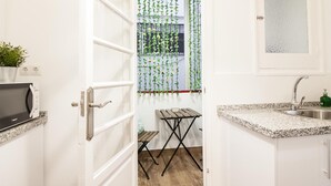 Eine Küche mit weißen Schränken, einer Granit Arbeitsplatte, einer Edelstahl-Spüle, einer Mikrowelle, einem kleinen Holztisch und einer hängenden Pflanze.