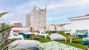 Eine Dachterrasse im Freien mit mehreren Sitzbereichen, darunter Sofas und Bänke, umgeben von Kunstgrasanlage.