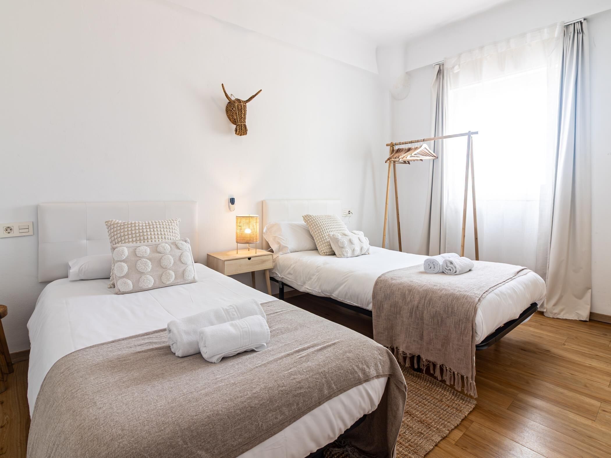 A hotel room with two beds, a wall-mounted bull head decoration, a bedside lamp, and a window with sheer curtains.