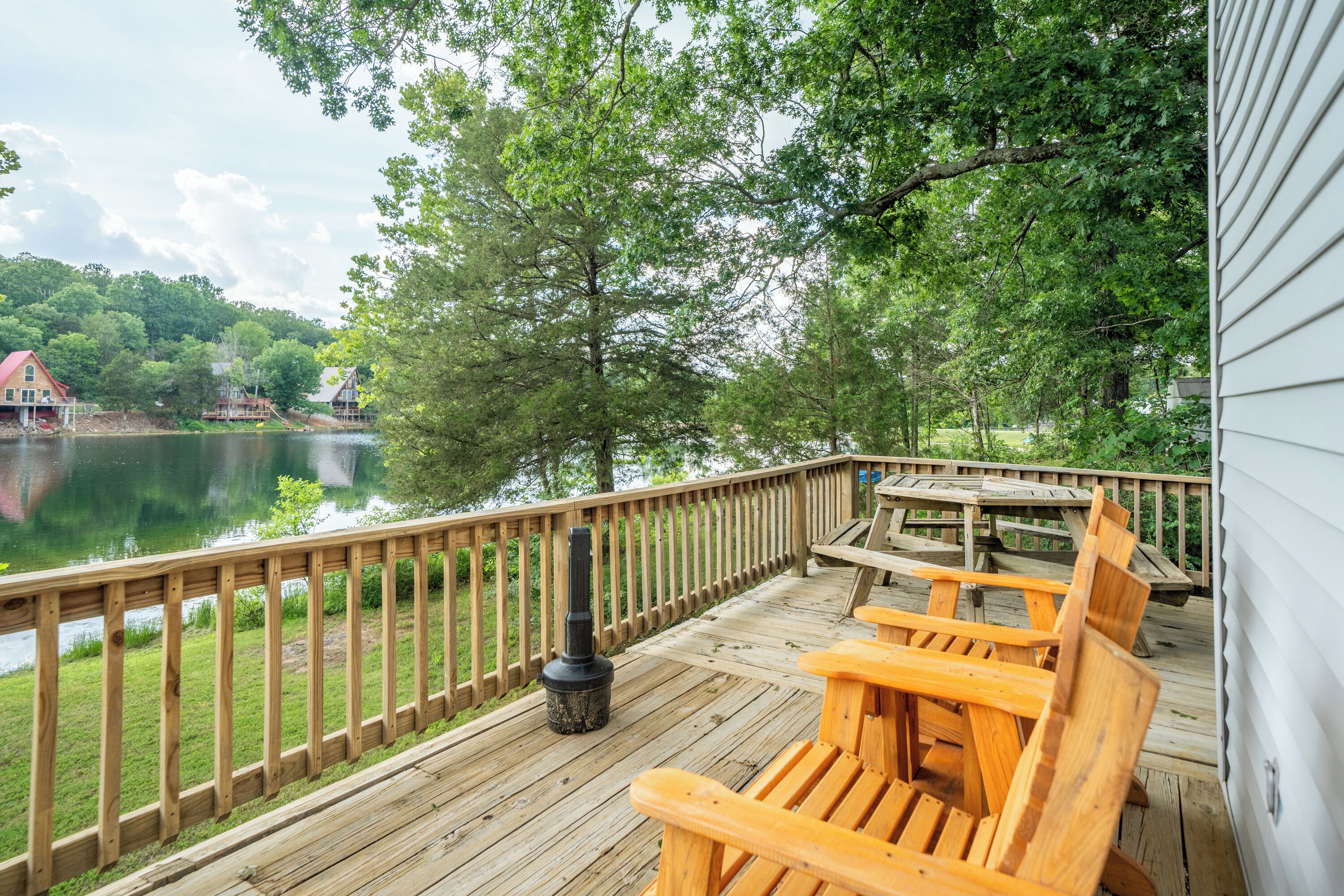 Un terrazza in legno con vista su un lago, circondata da alberi e una casa.