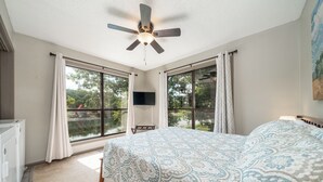 Ein Schlafzimmer mit einem Bett, einem Deckenventilator, einem Fernseher und großen Fenstern.