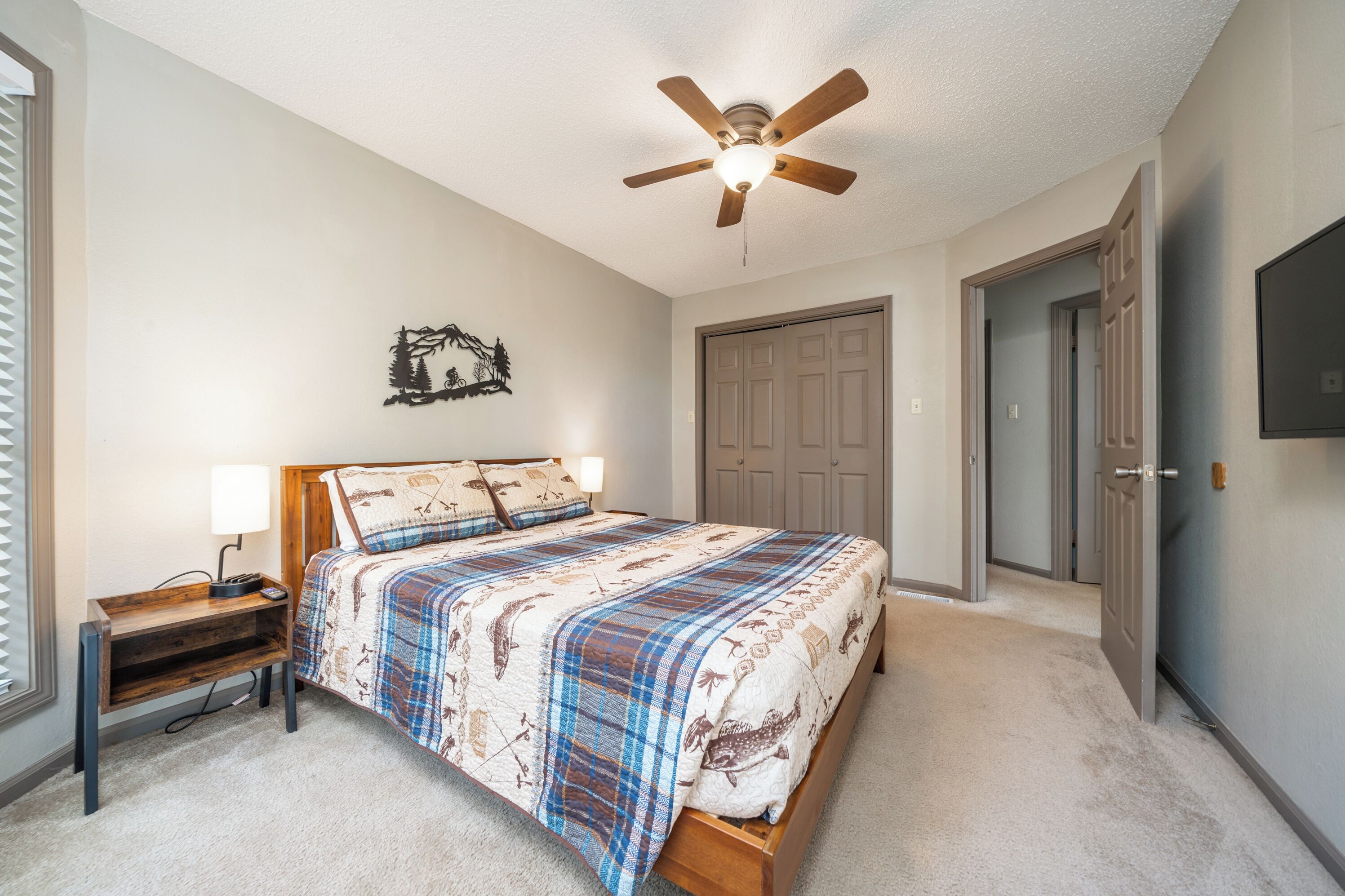 A bedroom with a bed, a nightstand, a ceiling fan, and a wall-mounted TV.