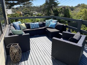 Une terrasse dotée d’un ensemble de meubles de jardin en rotin foncé, de plusieurs coussins et d’une chaise en rotin.