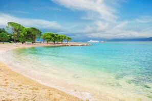 A beach with clear turquoise water, sandy shore, and green trees. - Studio Paula 1 300m From Sea (Crikvenica)